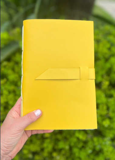 Caderno amarelo segurado ao ar livre, com detalhe de fechamento na capa